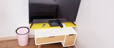A small TV stand with a flat-screen TV, a remote control, and a power strip.