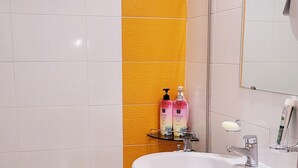 Et badeværelse med en hvid vask, toilet, bruser og et spejl. Der er to shampoo flasker på hylden.