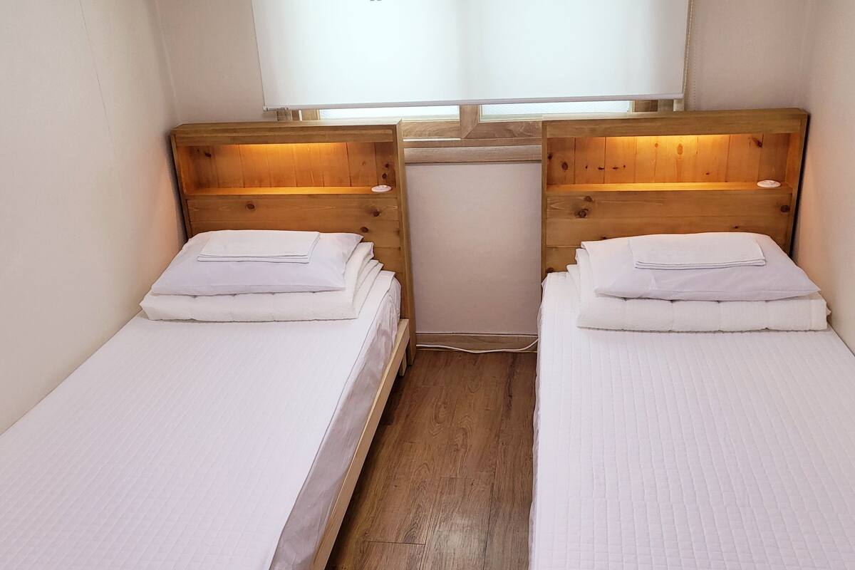 Two single beds with wooden headboards and white bedding, in a narrow room with a window above.