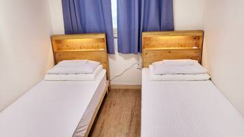A room with two single beds, wooden headboards, white bedding, and a power outlet on the wall.