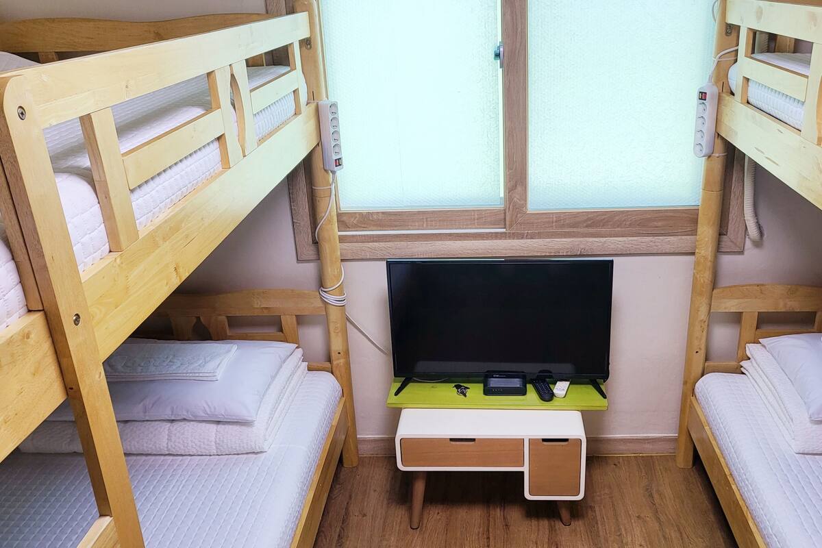 A bunk bed room with a desk, a TV, and a window.