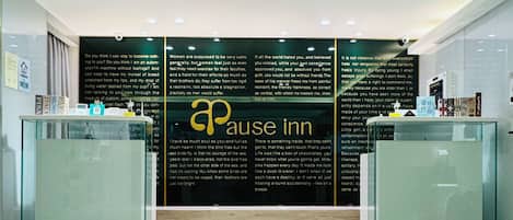 Zona de recepción con una pared negra que muestra texto y el logotipo de 'Pause Inn'.