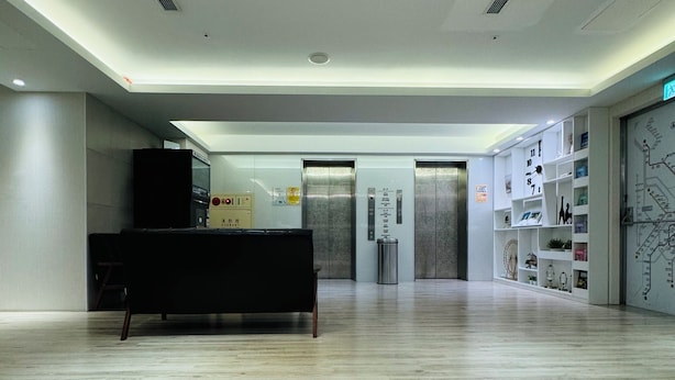 A spacious lobby with a reception desk, elevators, and a wall with a map and shelves. - APause Inn (Taipei)
