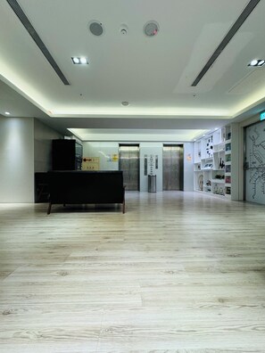 A spacious lobby with a reception desk, elevators, and a wall with a map and shelves. - APause Inn (Taipei)