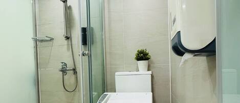 Un baño moderno con cabina de ducha de vidrio, inodoro con panel de control, secador de manos y una pequeña planta en maceta.