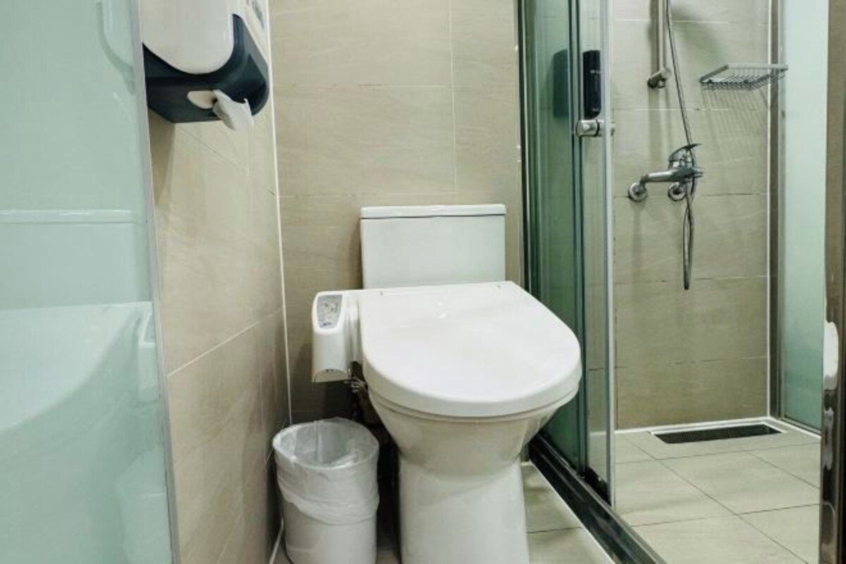A modern bathroom with a toilet, a trash bin, and a glass-enclosed shower area.