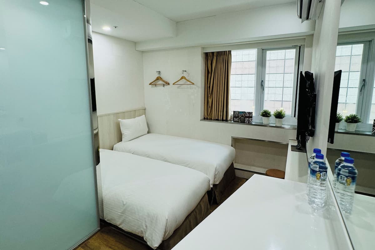 Une chambre d’hôtel avec deux lits, un bureau blanc, un miroir et une fenêtre avec des rideaux.