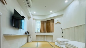 A hotel room with a tatami mat floor, a flat-screen TV mounted on the wall, a window with curtains, and a bed with neatly folded white linens. - APause Inn (Taipei)