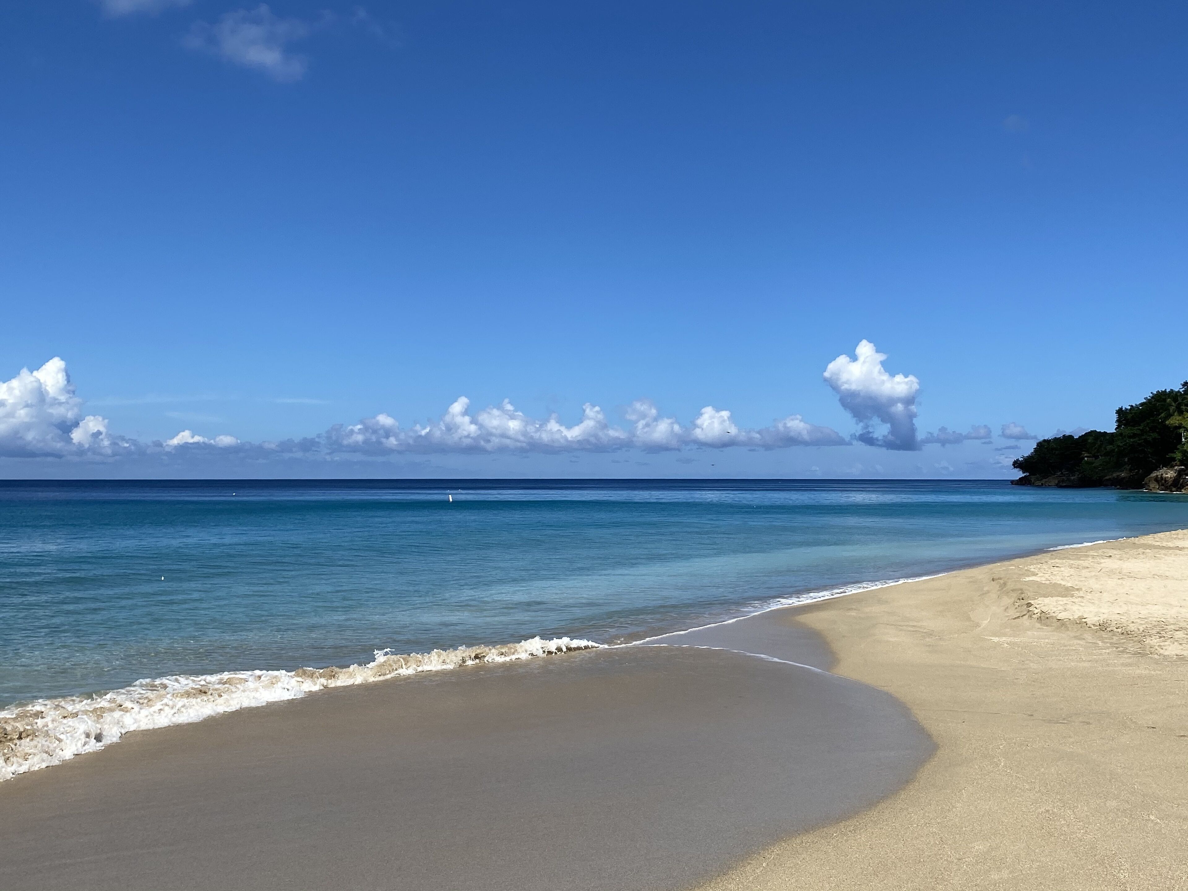 A beach with clear blue water, a sandy shore, and a distant rocky outcrop.