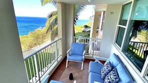 A balcony with a view of the ocean, two lounge chairs, a sofa, and a small table.