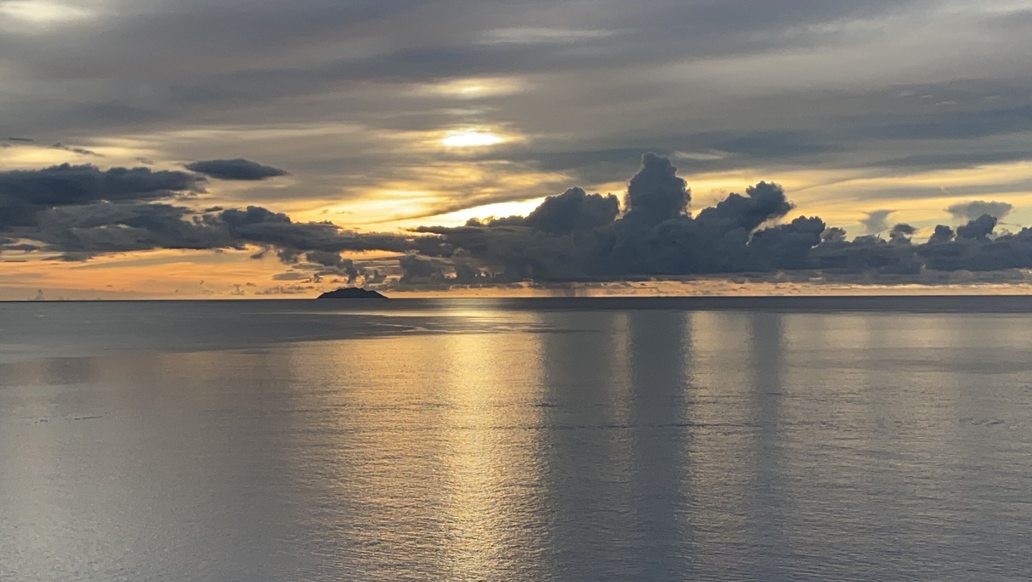 Une mer calme, avec un coucher de soleil et des nuages à l’horizon.