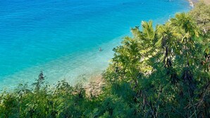 A coastal view with clear blue waters, a sandy beach, and a pier extending into the sea.