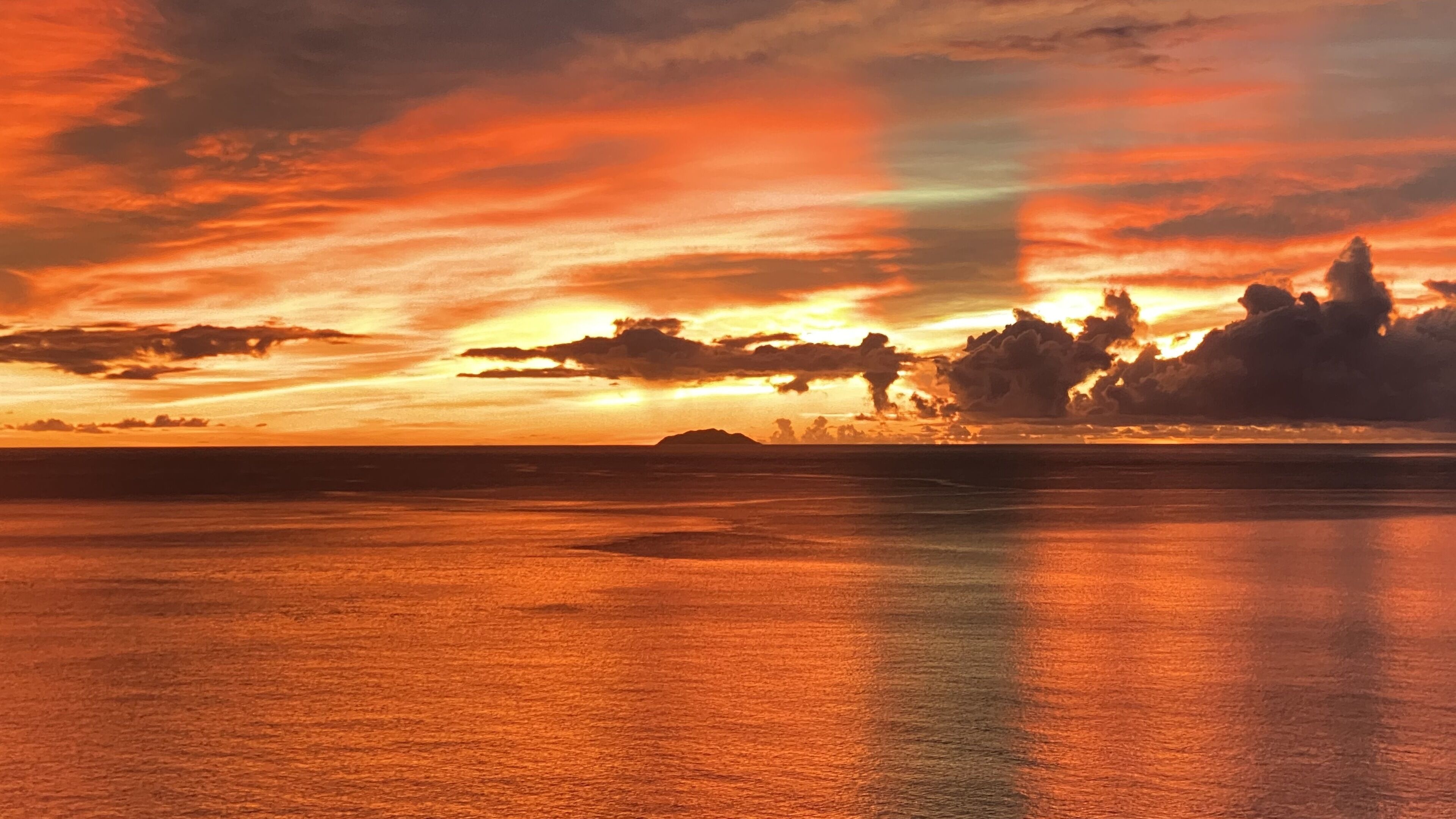 Un atardecer sobre un mar tranquilo con una masa de tierra a lo lejos.