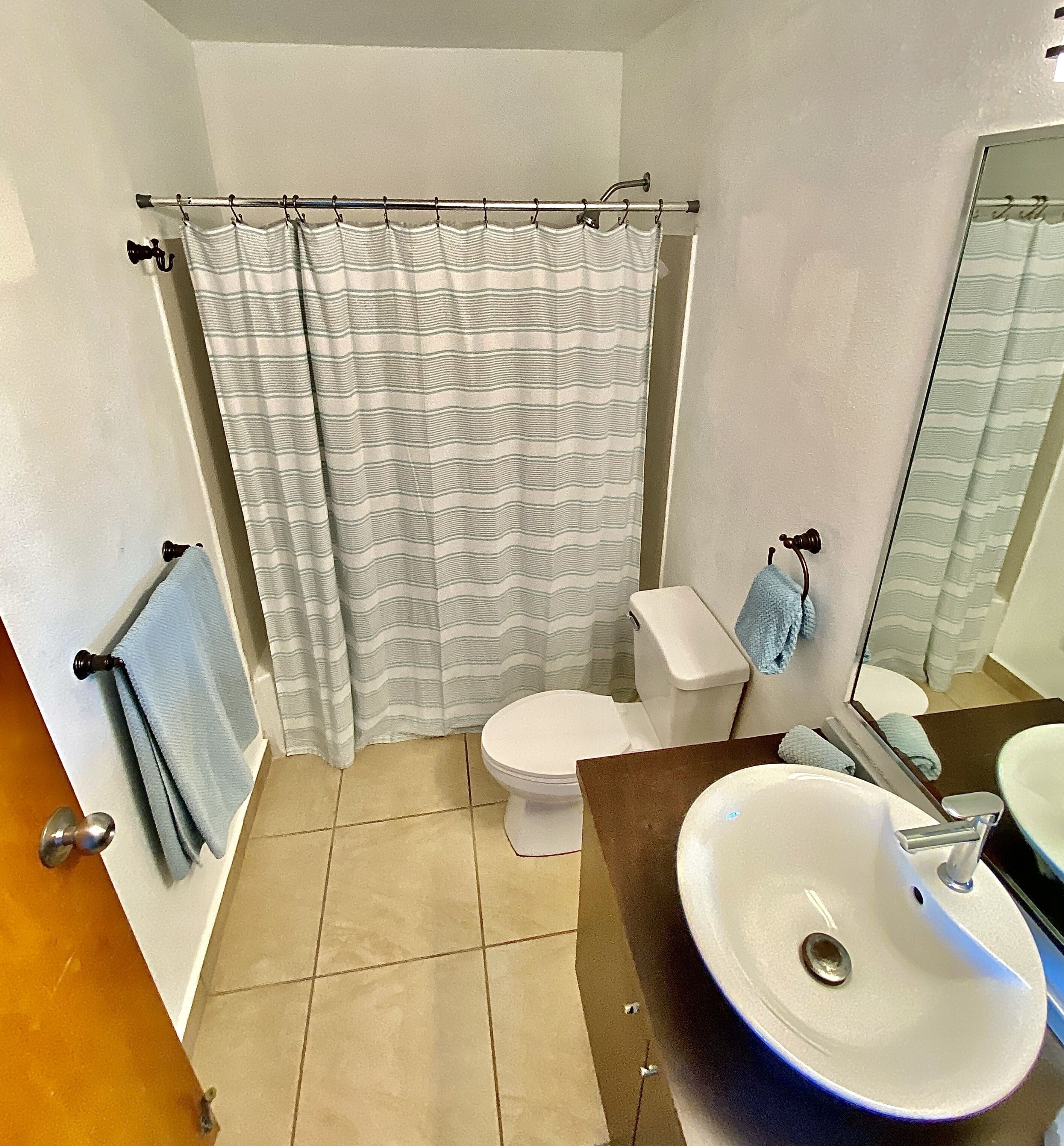 Un baño con cortina de ducha, inodoro, lavamanos y toallero.