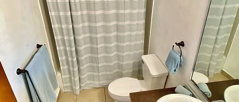 Un baño con cortina de ducha, inodoro, lavamanos y toallero.