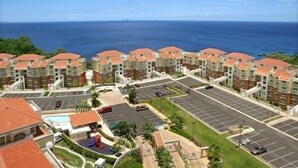 A coastal hotel with multiple buildings, a parking lot, and a swimming pool.