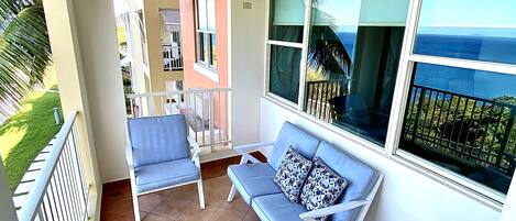 A balcony with two blue lounge chairs, a small table, and a view of the ocean.