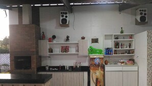 A kitchen with a built-in oven, bar stools, shelves with various items, and a refrigerator with a milk advertisement. - House in farmhouse with all structure of leisure and comfort (Mosqueiro (Condomínio Morada do Rio))