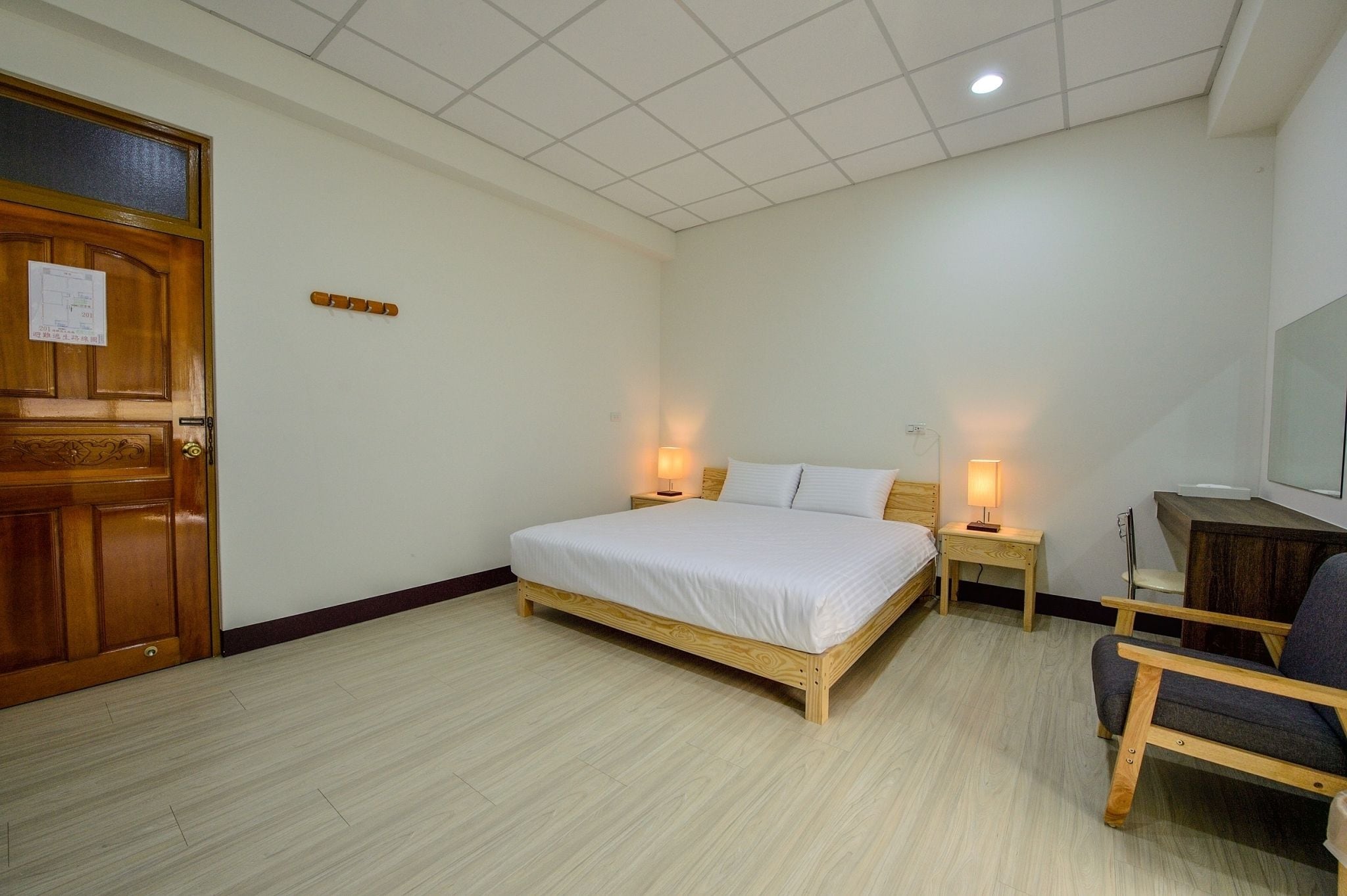 A bedroom with a wooden bed, two bedside tables with lamps, a wooden chair, and a wooden wardrobe.