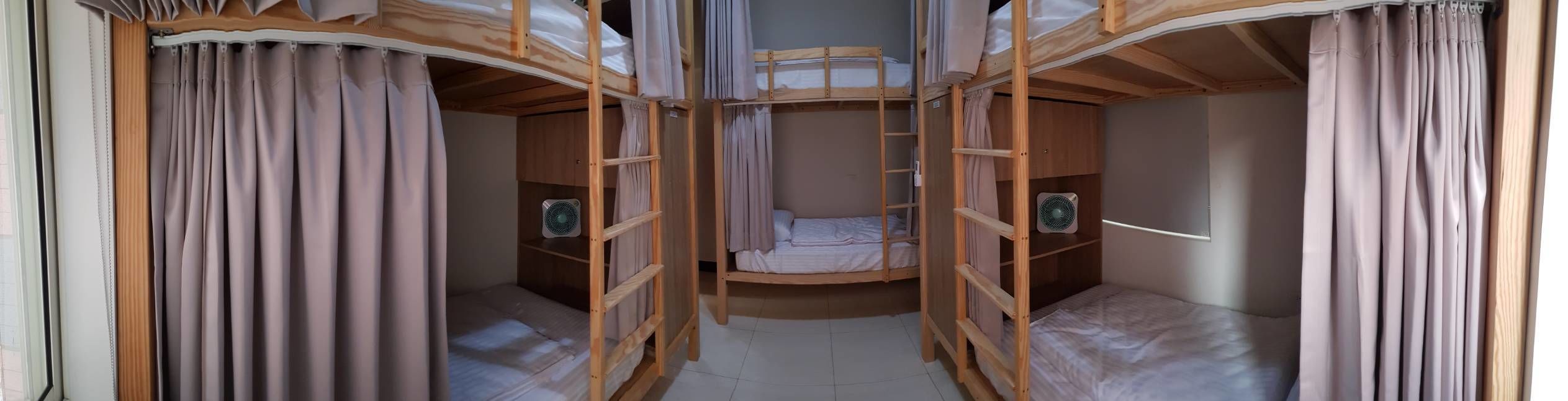 A bunk bed room with curtains, a ladder, and two fans.