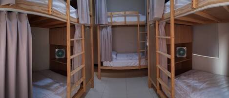 Habitación con literas, cortinas, una escalera y dos ventiladores.