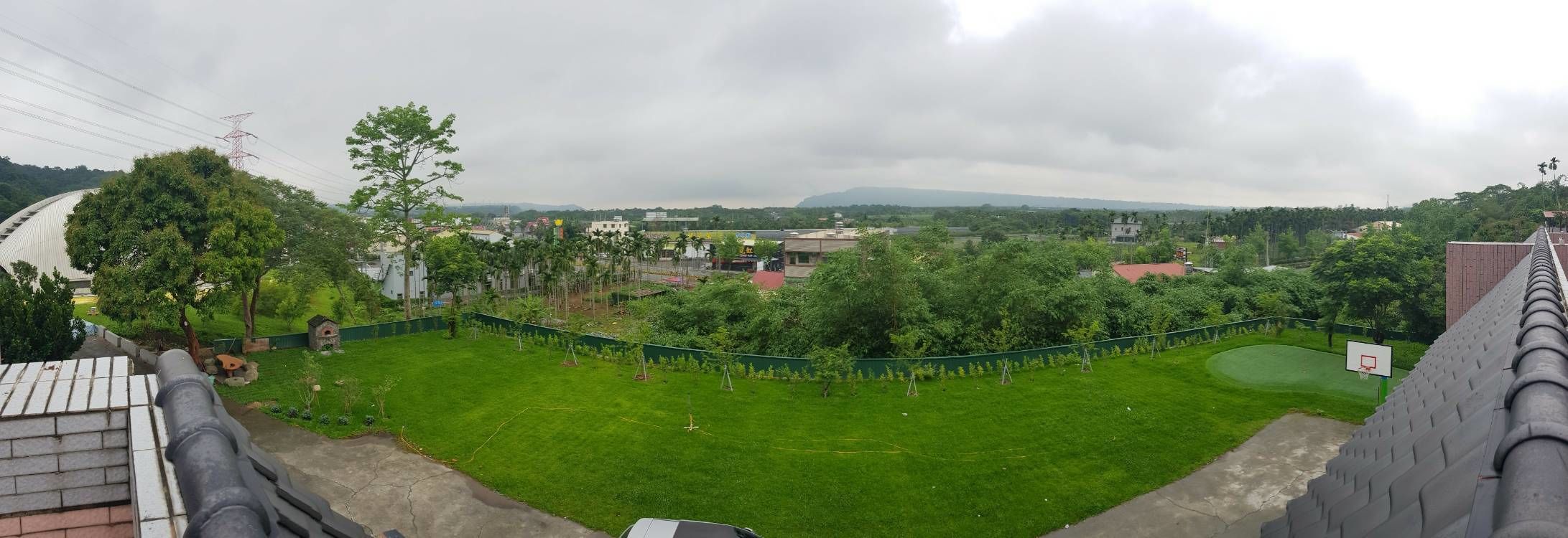 Un barrio residencial con césped verde, un aro de baloncesto y vistas a edificios y colinas distantes.