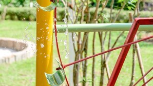 Une structure verticale jaune, d’où s’écoule de l’eau par un bec verseur, et qui est entourée de barres de métal rouges.