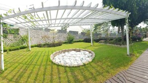 Un jardin agrémenté d’une pergola blanche, de murs en pierre et d’un élément décoratif circulaire en pierre.