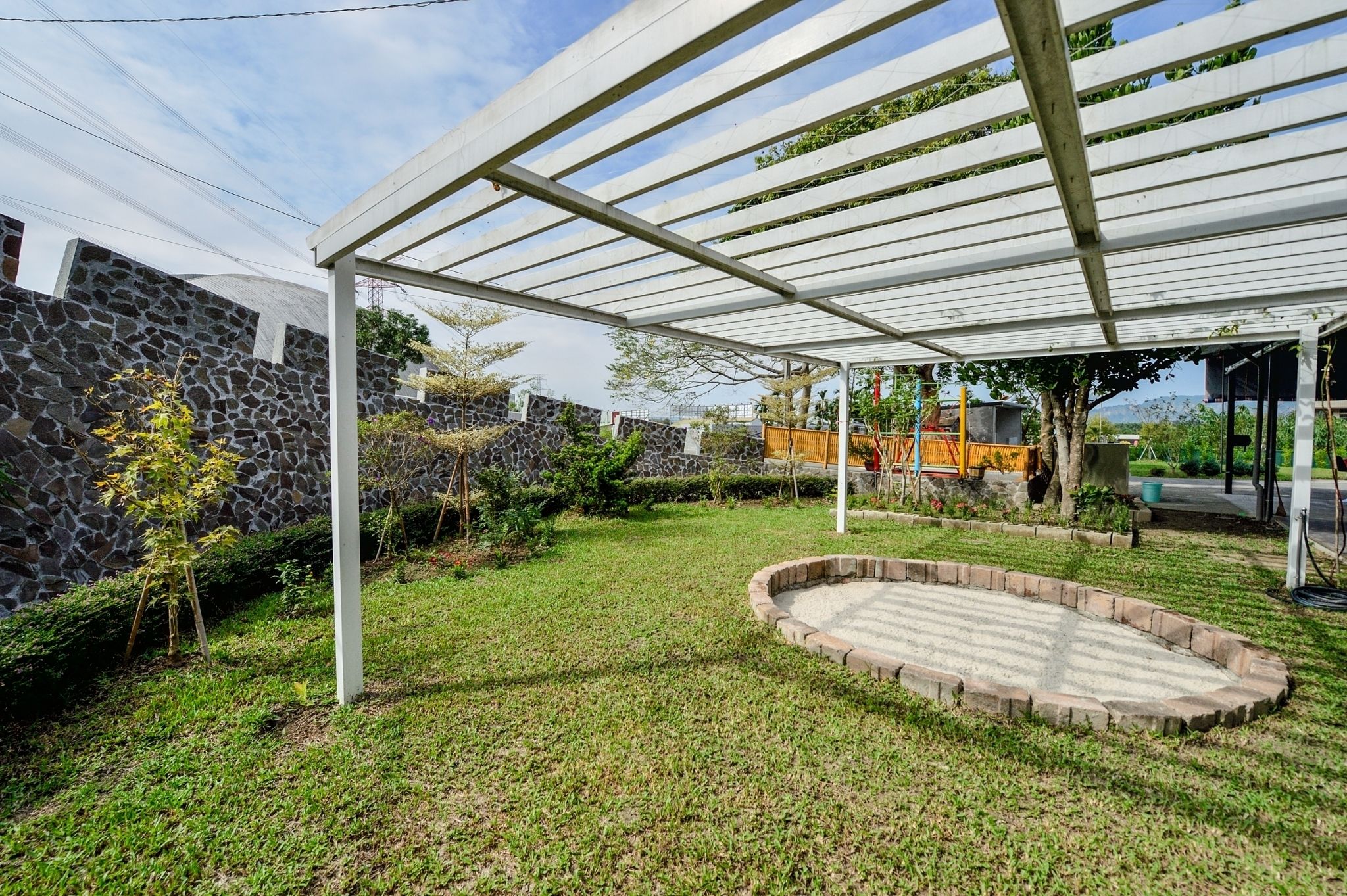 A covered outdoor area with a stone wall, a circular stone patio, and a pergola structure.