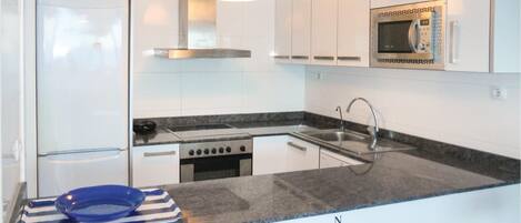 A modern kitchen with white cabinets, a stainless steel range hood, a built-in microwave, a double sink, and a stove.