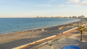 Um calçadão costeiro com uma praia de pedras, um corrimão de metal e uma vista ampla do mar.