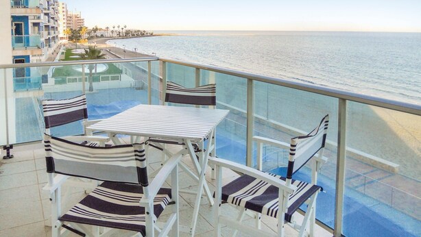 Varanda com mesa e cadeiras, vista para uma praia e oceano.