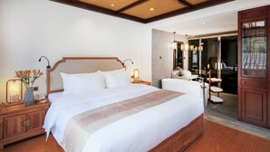 Un dormitorio amplio con una cama grande, cabecera de madera, mesitas de noche con lámparas y un baño visible a través de una puerta abierta.
