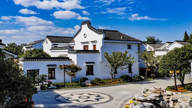 Un edificio tradicional blanco con tejado de tejas, rodeado de follaje y un cielo azul despejado.