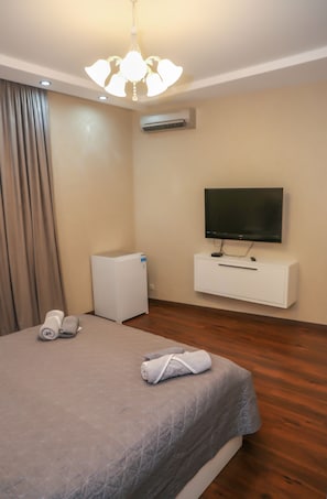 Une chambre d’hôtel avec un lit, un téléviseur fixé sur un meuble blanc, un climatiseur mural et un luminaire au plafond.