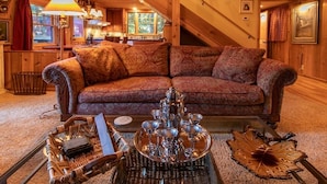 Un salon chaleureux avec un canapé à motifs, une table basse en verre agrémentée d’objets décoratifs et un coin repas avec des meubles en bois.