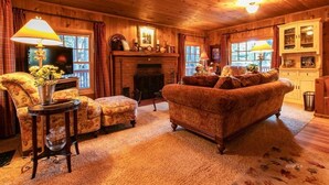 Un salon chaleureux avec une cheminée, des murs en bois, un canapé, un fauteuil et un téléviseur.