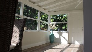 A room with a large window, wicker furniture, and a vase with flowers.