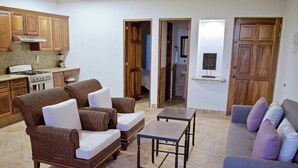 A living room with wicker furniture, a coffee table, and a sofa. There is a kitchen area with wooden cabinets and a stove. - "Ola",  One bedroom. You can walk to Beach and Restaurants (Punta de Mita)