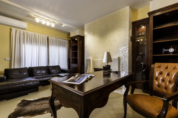 A living room with a dark brown leather sofa, a wooden coffee table with a magazine, a lamp, and a leather armchair.