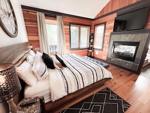 Un dormitorio con una cama grande, chimenea, paredes de madera y una ventana con cortinas.