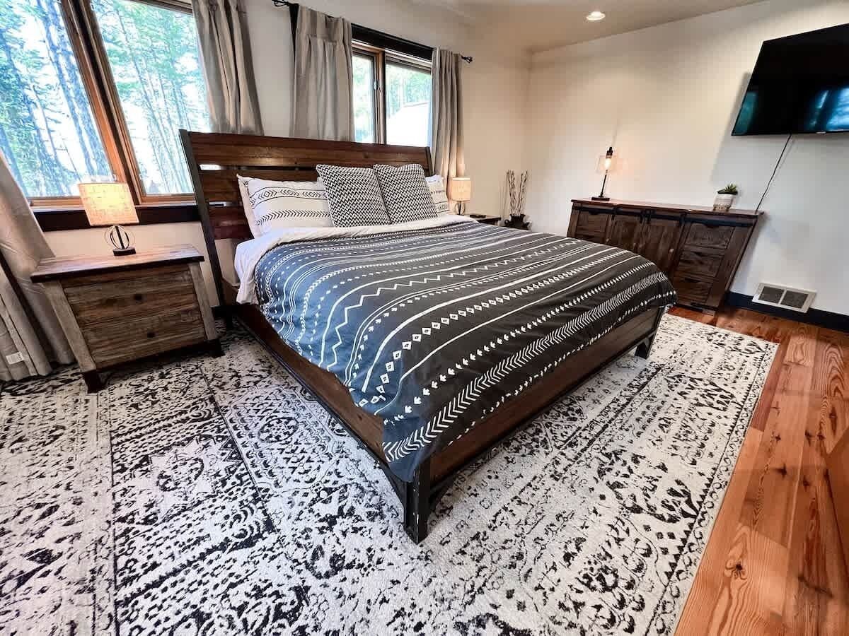 A bedroom with a large bed, wooden headboard, a TV, and a nightstand with a lamp.