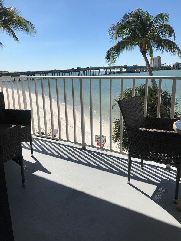 A balcony with wicker furniture overlooking a beach and a bridge. - Beachfront! Remodeled! Lovers Key Beach Club #103 (Fort Myers Beach)
