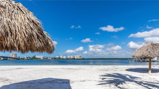 Una playa de arena blanca, una sombrilla de paja y un cielo azul despejado.