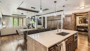 A modern kitchen with a large island, wooden cabinets, and pendant lighting.
