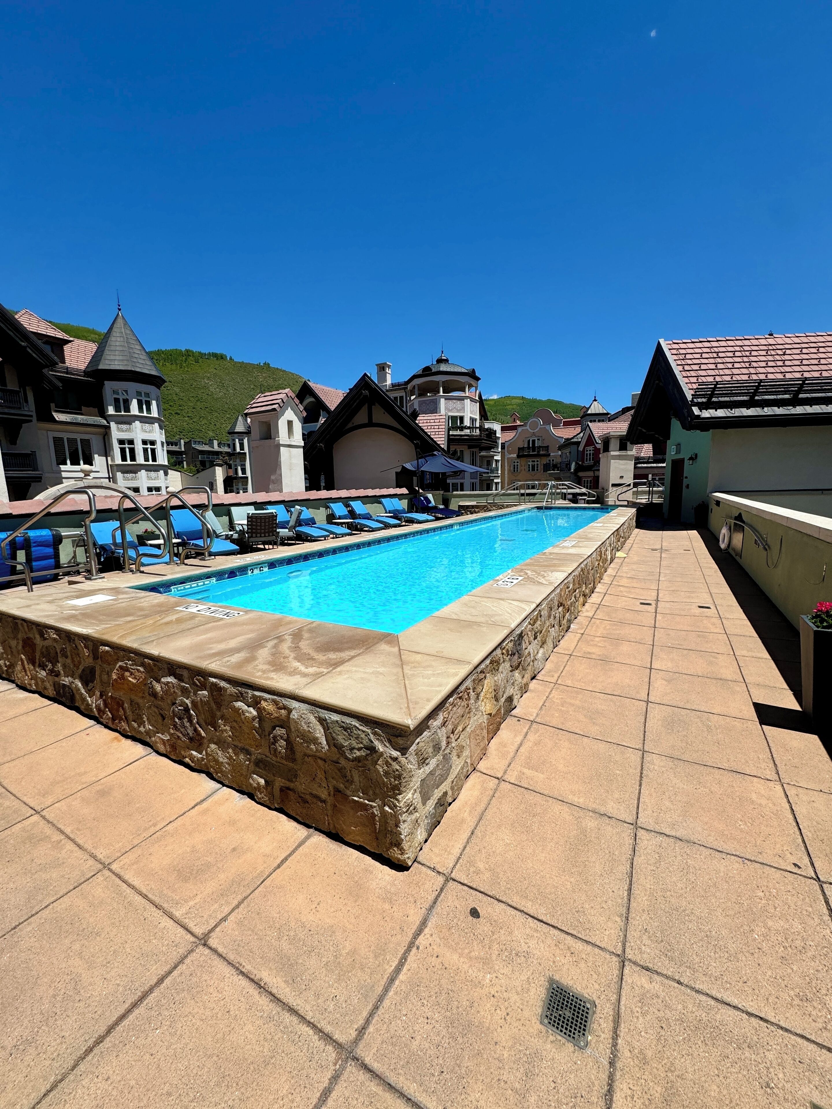 A swimming pool with lounge chairs, stone walls, and traditional European architecture.