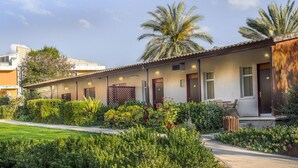 Una hilera de edificios de un solo piso con un jardín delantero, con palmeras y arbustos diversos.