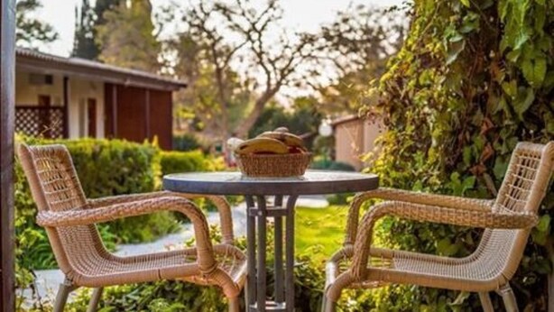 Una mesa redonda con sillas de mimbre, una cesta de pan y vistas a una casa y follaje verde.
