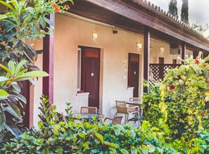 A building with a covered patio area, featuring a table and chairs, surrounded by lush greenery and a wooden fence. - Kibbutz Mashabei Sade Country Lodging (Ramat Negev)