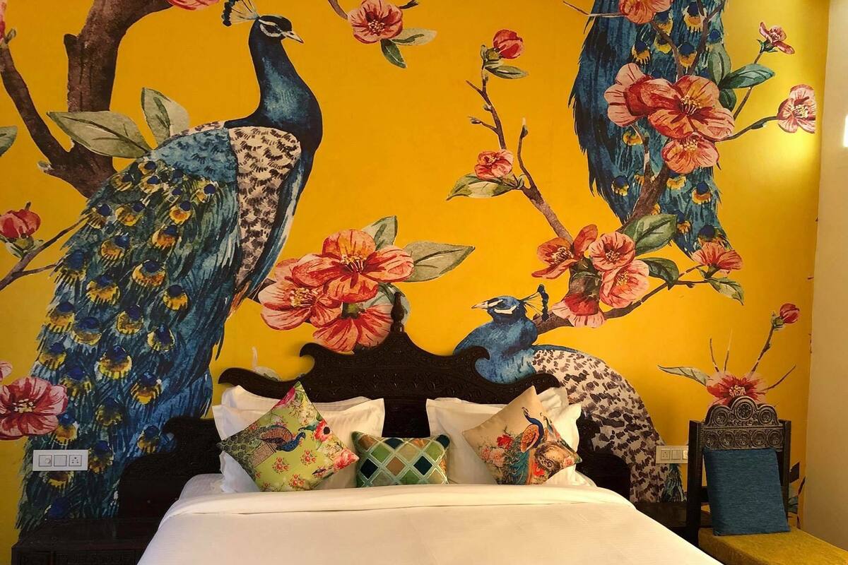 Une chambre à coucher avec un lit, des oreillers et une fresque murale représentant des paons et des fleurs.